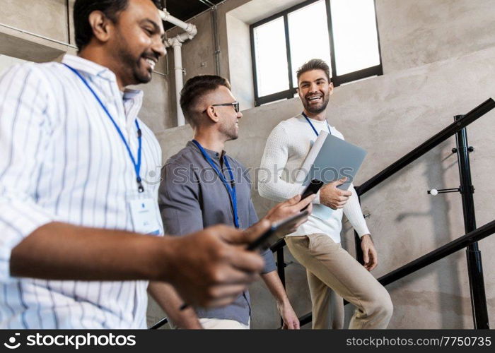 business, people and corporate concept - men with conference badges, folder, tablet pc computer and smartphone walking up office stairs. men with conference badges walking upstairs