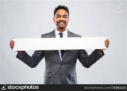 business, people and corporate concept - smiling indian businessman with white banner over grey background. smiling indian businessman with white banner