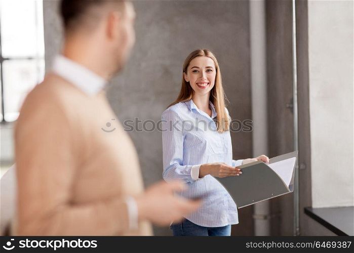 business, people and corporate concept - smiling woman with folder talking to colleague at office. woman with folder talking to colleague at office