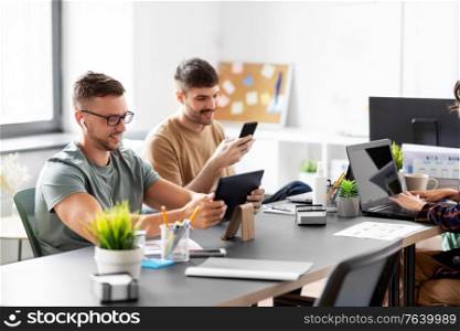 business, people and corporate concept - team of startuppers or ui designers with gadgets working at office. business team or startuppers working at office
