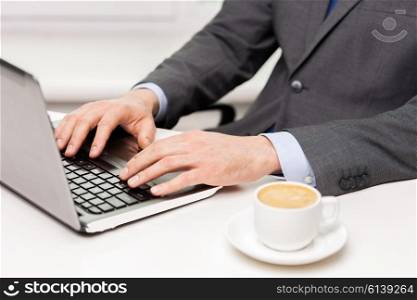 business, people and drinks concept - close up of businessman with coffee cup and laptop at office