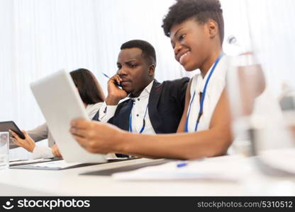 business, people and education concept - african american businessman and businesswoman with tablet pc computer at international conference. team with tablet pc at business conference