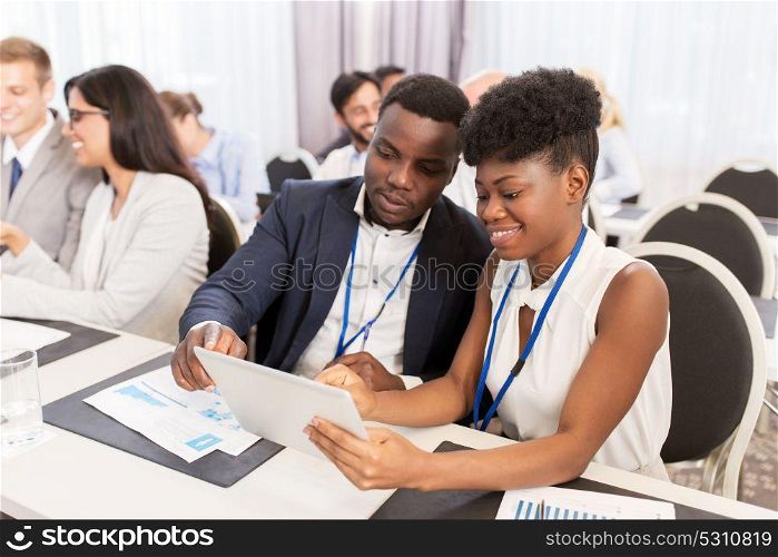 business, people and education concept - african american businessman and businesswoman with tablet pc computer at international conference. team with tablet pc at business conference