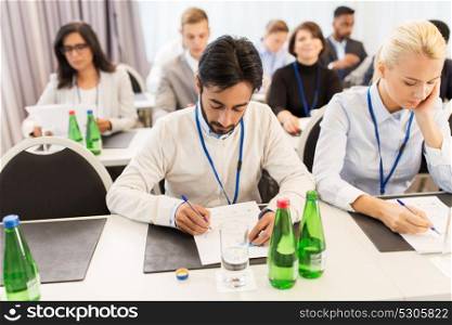 business, people and education concept - businessman and businesswoman with papers at international conference. businesspeople with papers at conference