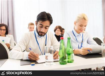business, people and education concept - businessman and businesswoman with papers at international conference. businesspeople with papers at conference