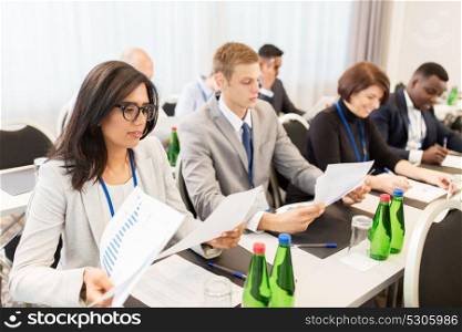 business, people and education concept - businesspeople with papers at international conference. businesspeople with papers at conference