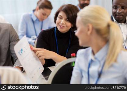 business, people and education concept - businesswoman showing document to colleague at international conference. business people at conference with papers