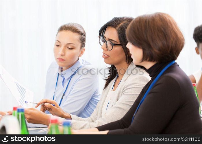 business, people and education concept - businesswoman showing document to colleague at international conference. businesswomen at international business conference