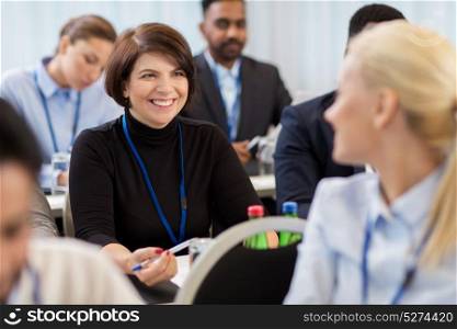 business, people and education concept - businesswoman talking to colleague at international conference. business people at conference with papers