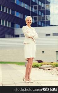 business, people and education concept - friendly young smiling businesswoman with crossed arms over office building