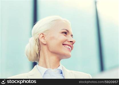 business, people and education concept - young smiling businesswoman over office building