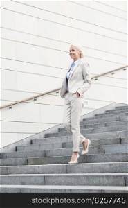 business, people and education concept - young smiling businesswoman walking down stairs outdoors