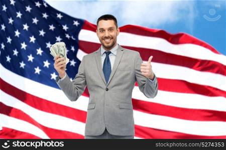 business, people and finances concept - smiling businessman with bundle of dollar cash money showing thumbs up over american flag background. happy businessman with american dollar money