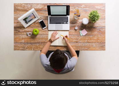 business, people and freelance concept - woman with laptop computer drawing to notebook at home or office table. woman drawing to notebook at home office