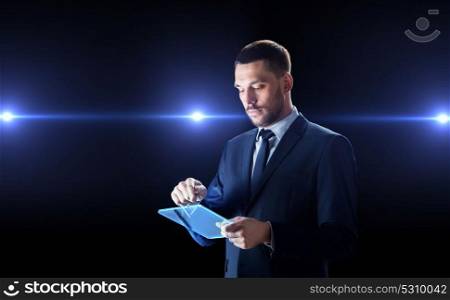 business, people and future technology concept - businessman in suit working with transparent tablet pc computer with laser lights over black background. businessman in suit with transparent tablet pc