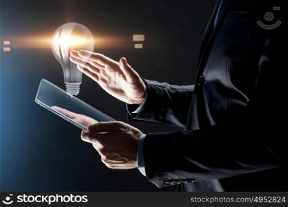 business, people and future technology concept - close up of businessman hands with transparent tablet pc computer and lightbulb projection over black background. close up of businessman with transparent tablet pc