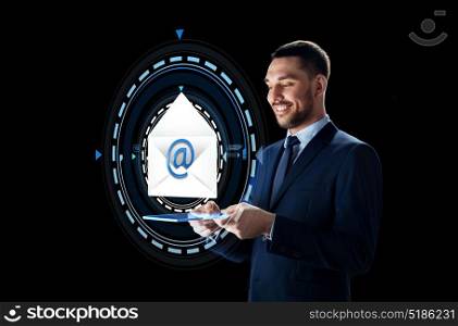 business, people and future technology concept - smiling businessman in suit working with transparent tablet pc computer and e-mail message hologram over black background. businessman with tablet pc and e-mail hologram