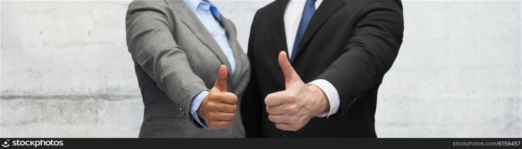 business, people and gesture concept - close up of businessman and businesswoman showing thumbs up over gray concrete wall background