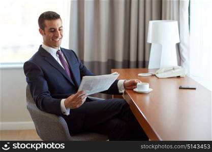 business, people and mass media concept - happy smiling businessman reading newspaper and drinking coffee at hotel room. businessman reading newspaper and drinking coffee