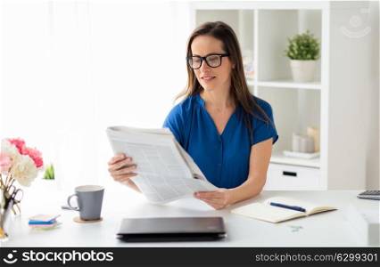 business, people and mass media concept - happy smiling businesswoman in glasses reading newspaper at office. businesswoman reading newspaper at office