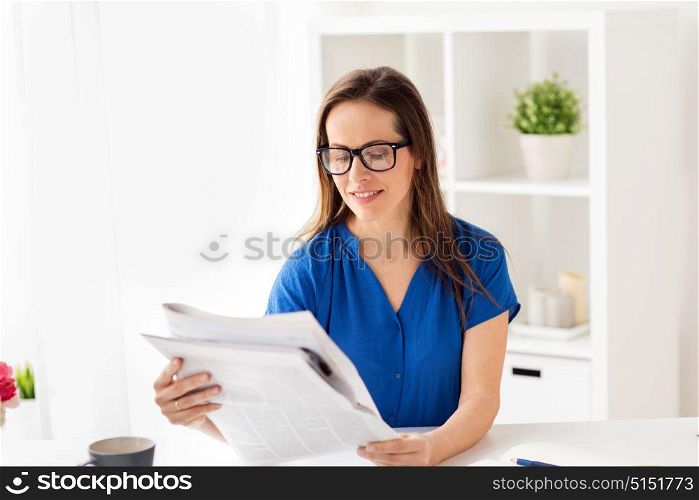 business, people and mass media concept - happy smiling woman in glasses reading newspaper at office. happy woman in glasses reading newspaper at office