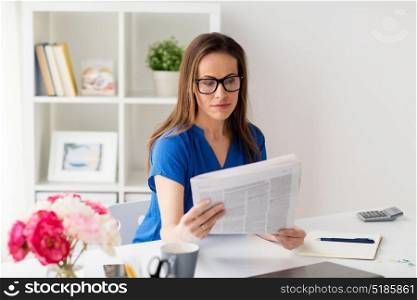 business, people and mass media concept - woman in glasses reading newspaper at office. woman in glasses reading newspaper at office