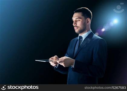 business, people and modern technology concept - businessman in suit working holding transparent tablet pc computer over black background with lens flare. businessman in suit with transparent tablet pc