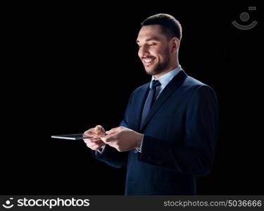 business, people and modern technology concept - smiling businessman in suit working with transparent tablet pc computer over black background. businessman in suit with transparent tablet pc