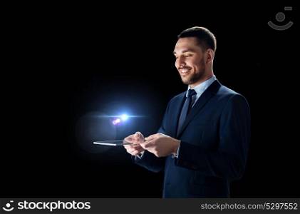 business, people and modern technology concept - smiling businessman in suit working with transparent tablet pc computer over black background. businessman in suit with transparent tablet pc