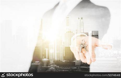 business, people and mortgage concept - close up of businessman holding keys over city with double exposure. close up of businessman holding keys