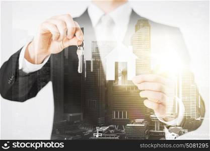 business, people and mortgage concept - close up of businessman holding keys and paper house over city with double exposure. close up of businessman holding keys and house