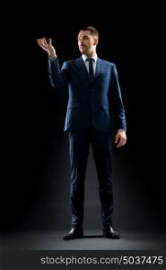 business, people and office concept - businessman in suit holding something invisible over black background. businessman in suit holding something invisible