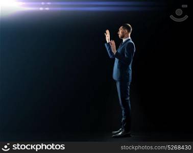 business, people and office concept - businessman in suit touching something invisible over black background with laser light. businessman in suit touching something invisible