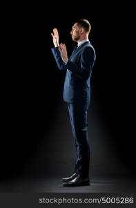 business, people and office concept - businessman in suit touching something invisible over black background. businessman in suit touching something invisible