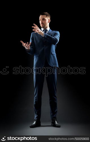 business, people and office concept - businessman in suit touching something invisible over black background. businessman in suit touching something invisible