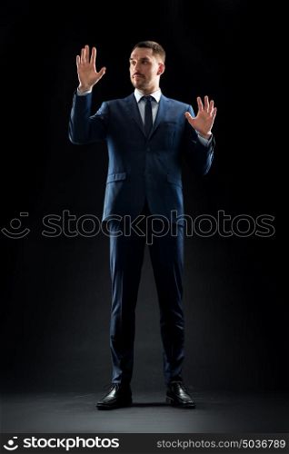 business, people and office concept - businessman in suit touching something invisible over black background. businessman in suit touching something invisible