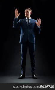 business, people and office concept - businessman in suit touching something invisible over black background. businessman in suit touching something invisible