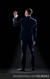 business, people and office concept - businessman in suit touching something invisible over black background. businessman in suit touching something invisible