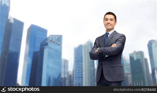 business, people and office concept - happy smiling businessman in dark grey suit over singapore city skyscrapers background