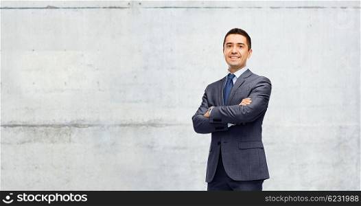 business, people and office concept - happy smiling businessman in dark grey suit over gray concrete wall background