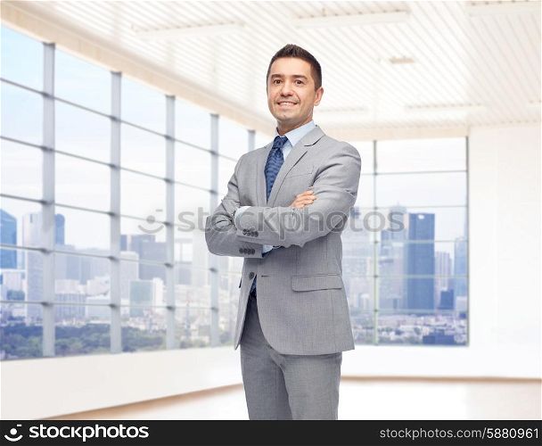 business, people and office concept - happy smiling businessman in suit over room and window with city view background