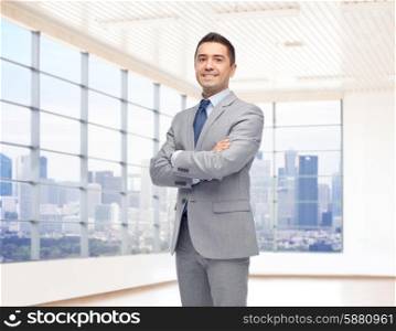 business, people and office concept - happy smiling businessman in suit over room and window with city view background