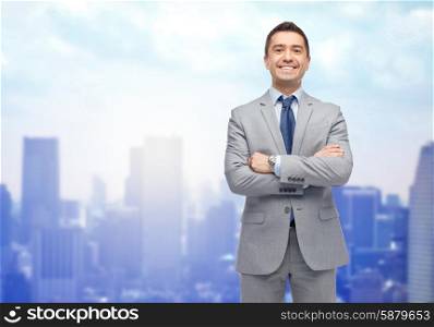 business, people and office concept - happy smiling businessman in suit over city background