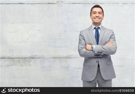 business, people and office concept - happy smiling businessman in suit over gray concrete wall background