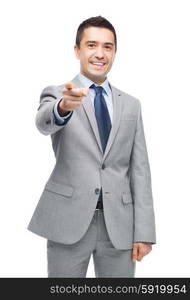 business, people and office concept - happy smiling businessman in suit pointing at you