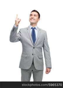 business, people and office concept - happy smiling businessman in suit pointing finger up