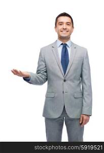 business, people and office concept - happy smiling businessman in suit showing something imaginary on empty palm