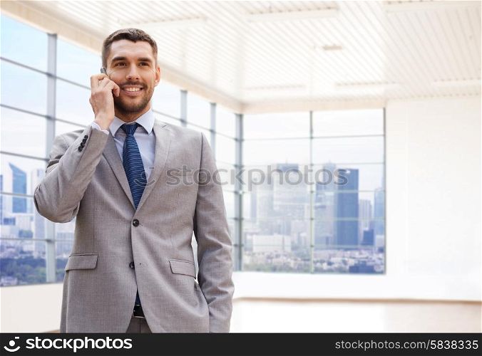 business, people and office concept - happy young businessman calling on smartphone over office room or new apartment background