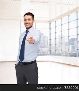 business, people and office concept - happy young businessman pointing finger at you over office room or new apartment background