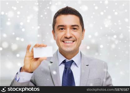business, people and office concept - smiling businessman in suit showing blank white visiting card over snow effect